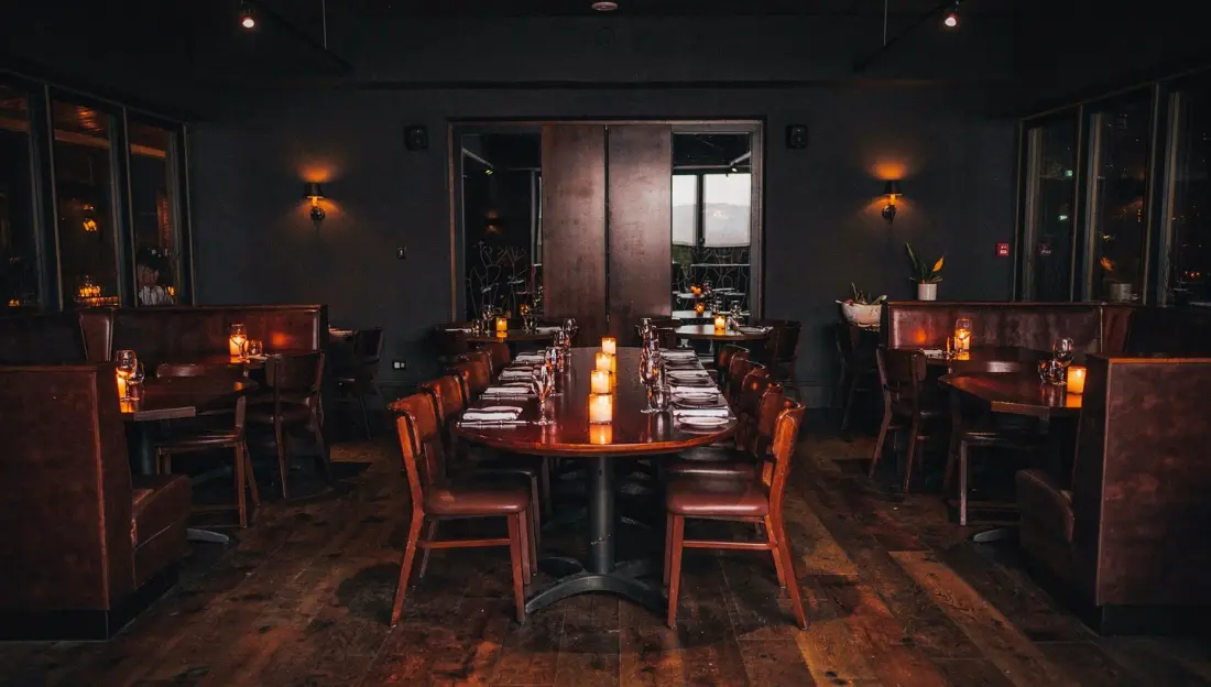Dining room with high-backed leather booths, candlelit tables set with wine glasses, and a backlit bar.