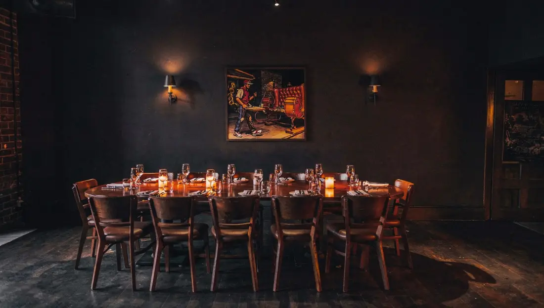 Private dining room with a long candlelit table, leather booths either side, and a window to the night.